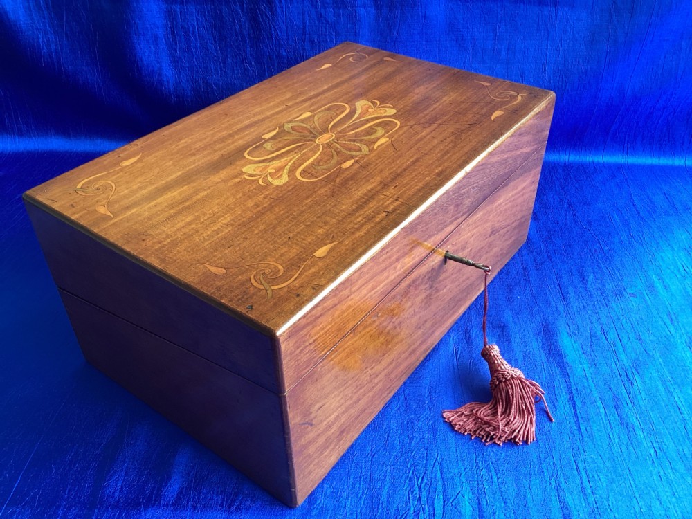 A rectangular dark walnut wooden writing slope featuring stylised floral marquetry inlay across the top lid and a key with a pink tassel in the front lock. View II