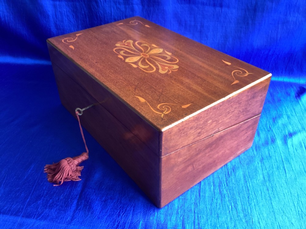 A rectangular dark walnut wooden writing slope featuring stylised floral marquetry inlay across the top lid and a key with a pink tassel in the front lock. View III