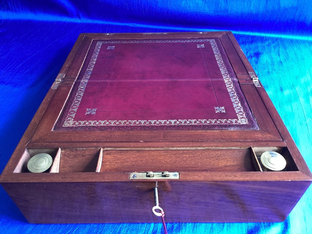 A rectangular dark walnut wooden writing slope featuring stylised floral marquetry inlay across the top lid and a key with a pink tassel in the front lock. View V