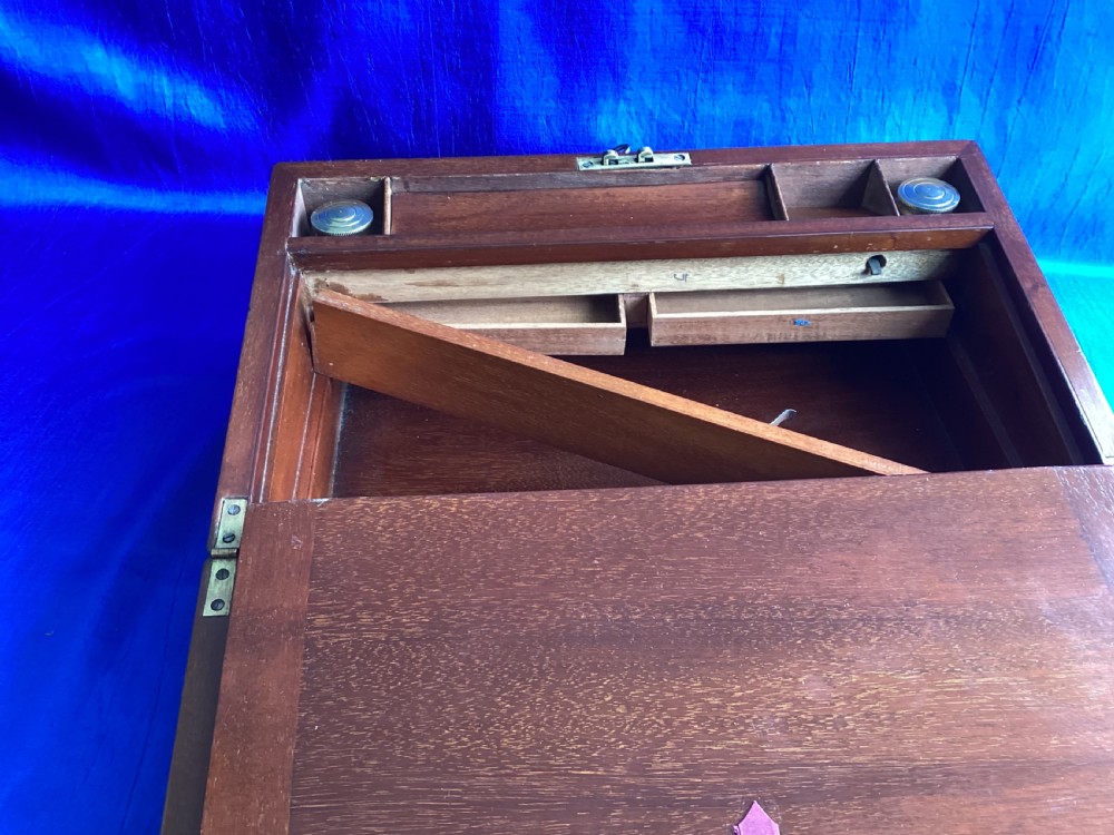 A rectangular dark walnut wooden writing slope featuring stylised floral marquetry inlay across the top lid and a key with a pink tassel in the front lock. View VI