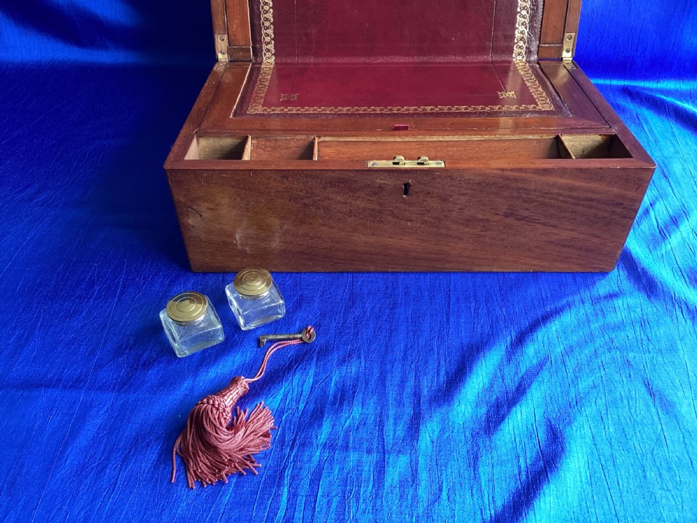 A rectangular dark walnut wooden writing slope featuring stylised floral marquetry inlay across the top lid and a key with a pink tassel in the front lock. View VIII