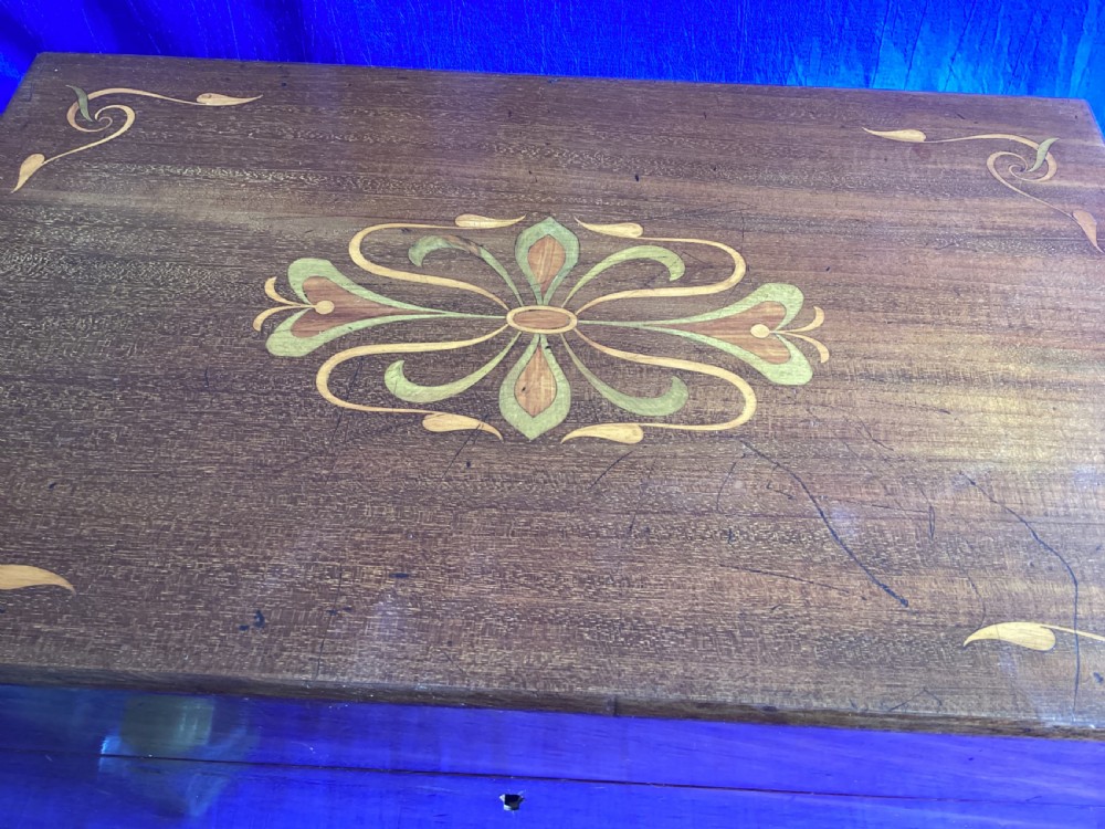 A rectangular dark walnut wooden writing slope featuring stylised floral marquetry inlay across the top lid and a key with a pink tassel in the front lock. View X