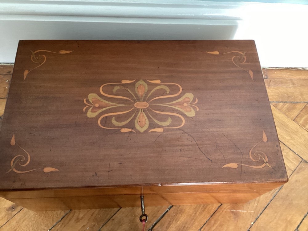 A rectangular dark walnut wooden writing slope featuring stylised floral marquetry inlay across the top lid and a key with a pink tassel in the front lock. View XI