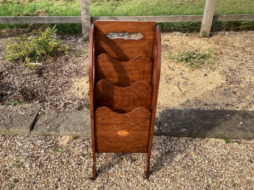 A floor-standing Edwardian oak magazine rack featuring three tiered sections, an integrated top handle aperture, and an oval marquetry shell inlay on the lower panel.