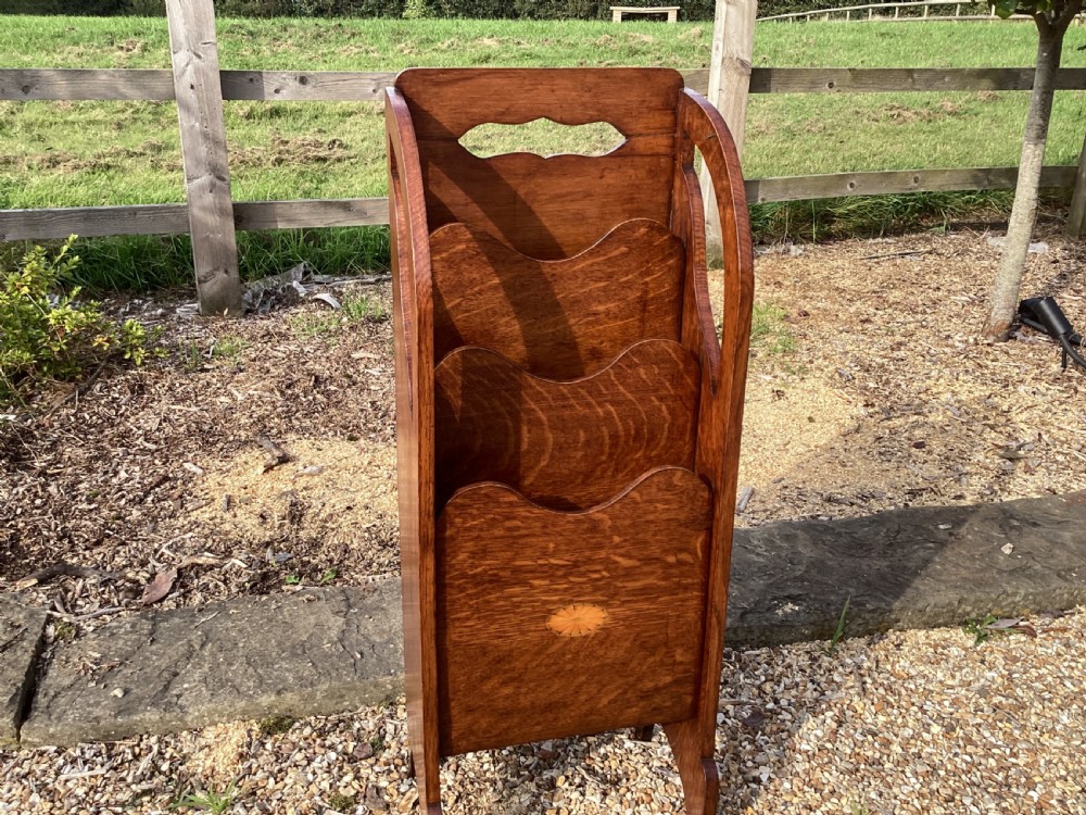 A floor-standing Edwardian oak magazine rack featuring three tiered sections, an integrated top handle aperture, and an oval marquetry shell inlay on the lower panel. View VII