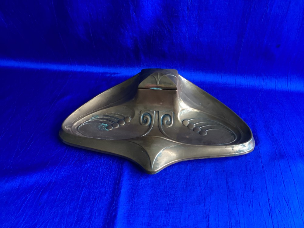 An antique Art Nouveau cast copper inkstand with a central hinged lid, contoured pen recesses, and embossed stylised botanical scrollwork.