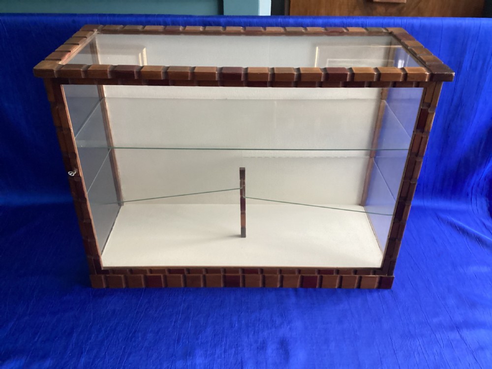 A rectangular Art Deco tabletop glass display case featuring notched wood framing and internal glass shelves.