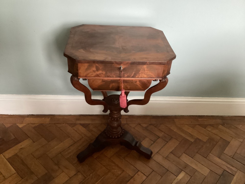 A Victorian flame mahogany sewing work table featuring a hinged top above a tapered work box, supported by curved S-scroll struts on a turned central pedestal with carved tripod legs. View II
