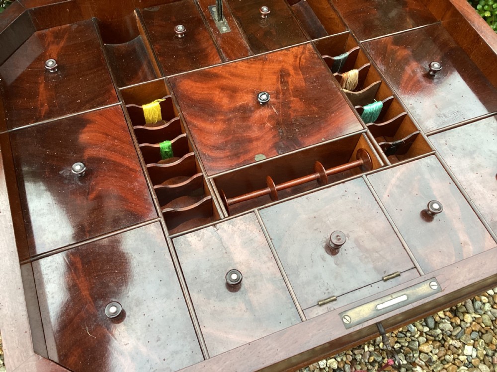 A Victorian flame mahogany sewing work table featuring a hinged top above a tapered work box, supported by curved S-scroll struts on a turned central pedestal with carved tripod legs. View V