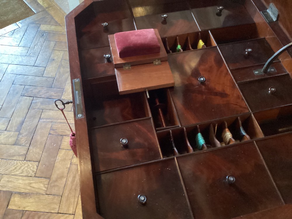A Victorian flame mahogany sewing work table featuring a hinged top above a tapered work box, supported by curved S-scroll struts on a turned central pedestal with carved tripod legs. View VI