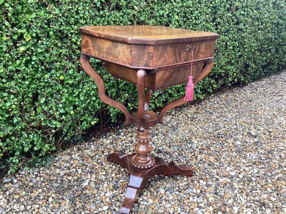 A Victorian flame mahogany sewing work table featuring a hinged top above a tapered work box, supported by curved S-scroll struts on a turned central pedestal with carved tripod legs. View VIII