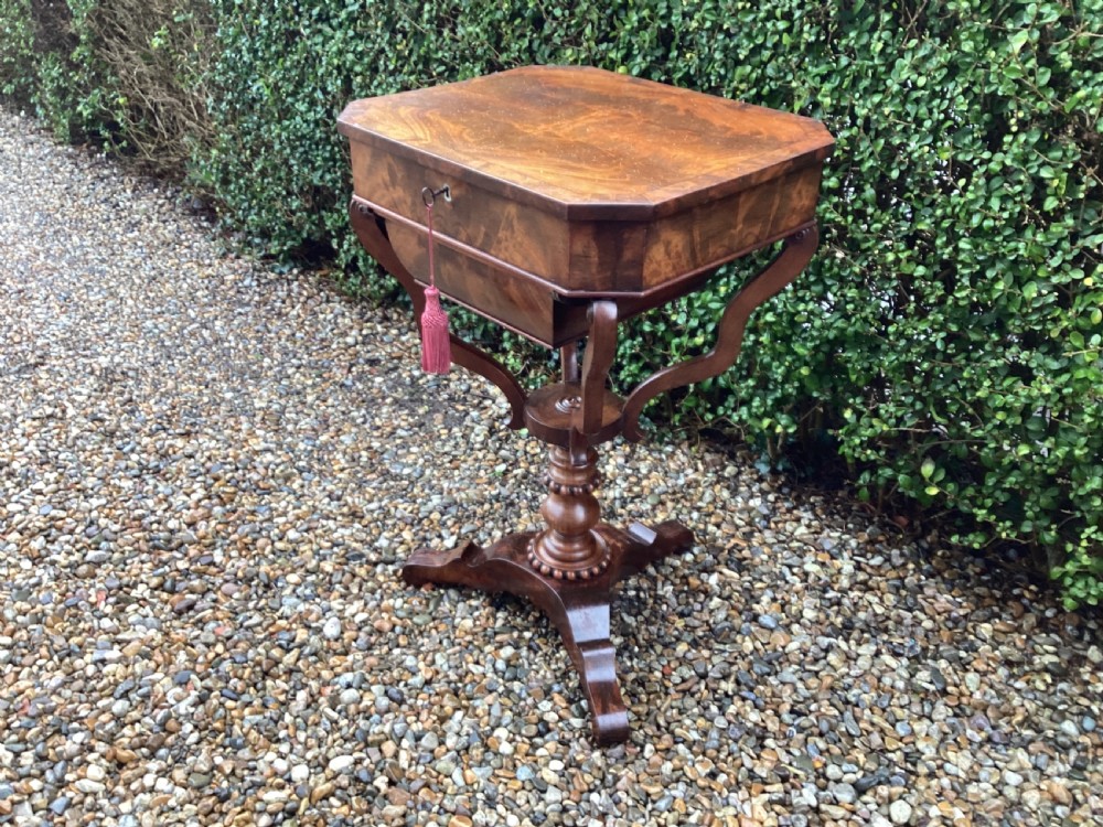 A Victorian flame mahogany sewing work table featuring a hinged top above a tapered work box, supported by curved S-scroll struts on a turned central pedestal with carved tripod legs. View IX