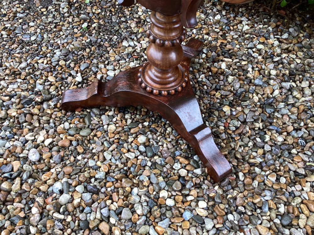 A Victorian flame mahogany sewing work table featuring a hinged top above a tapered work box, supported by curved S-scroll struts on a turned central pedestal with carved tripod legs. View X