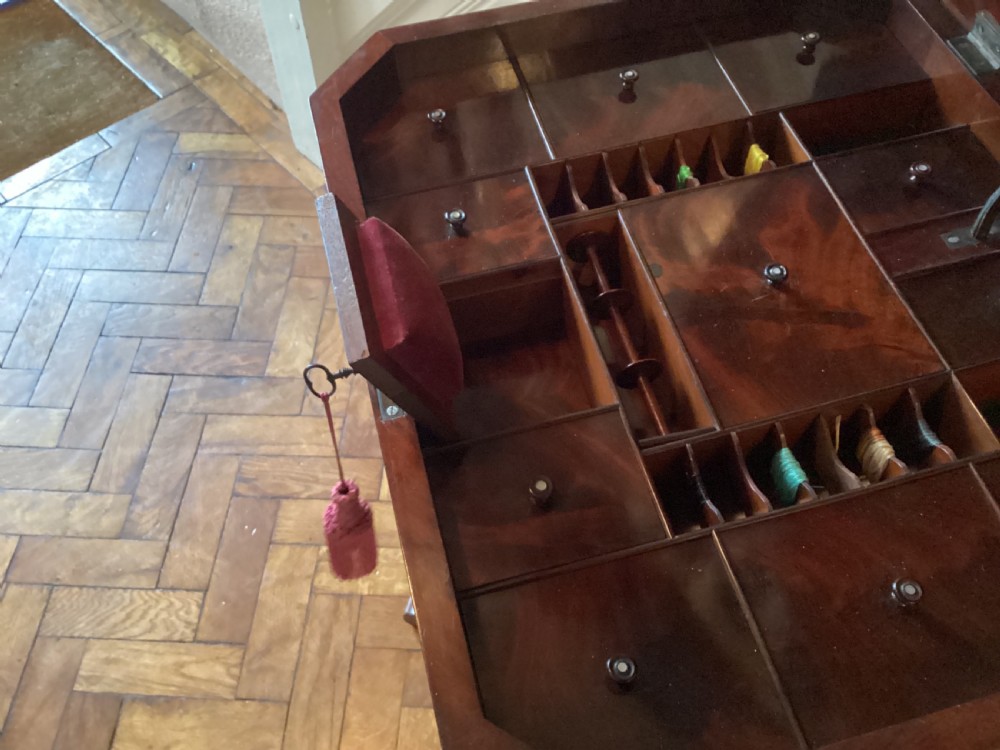 A Victorian flame mahogany sewing work table featuring a hinged top above a tapered work box, supported by curved S-scroll struts on a turned central pedestal with carved tripod legs. View XII