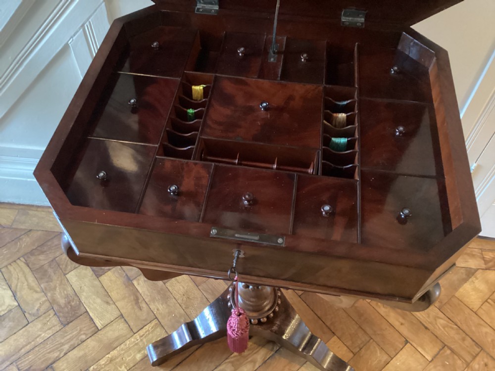 A Victorian flame mahogany sewing work table featuring a hinged top above a tapered work box, supported by curved S-scroll struts on a turned central pedestal with carved tripod legs. View XIII