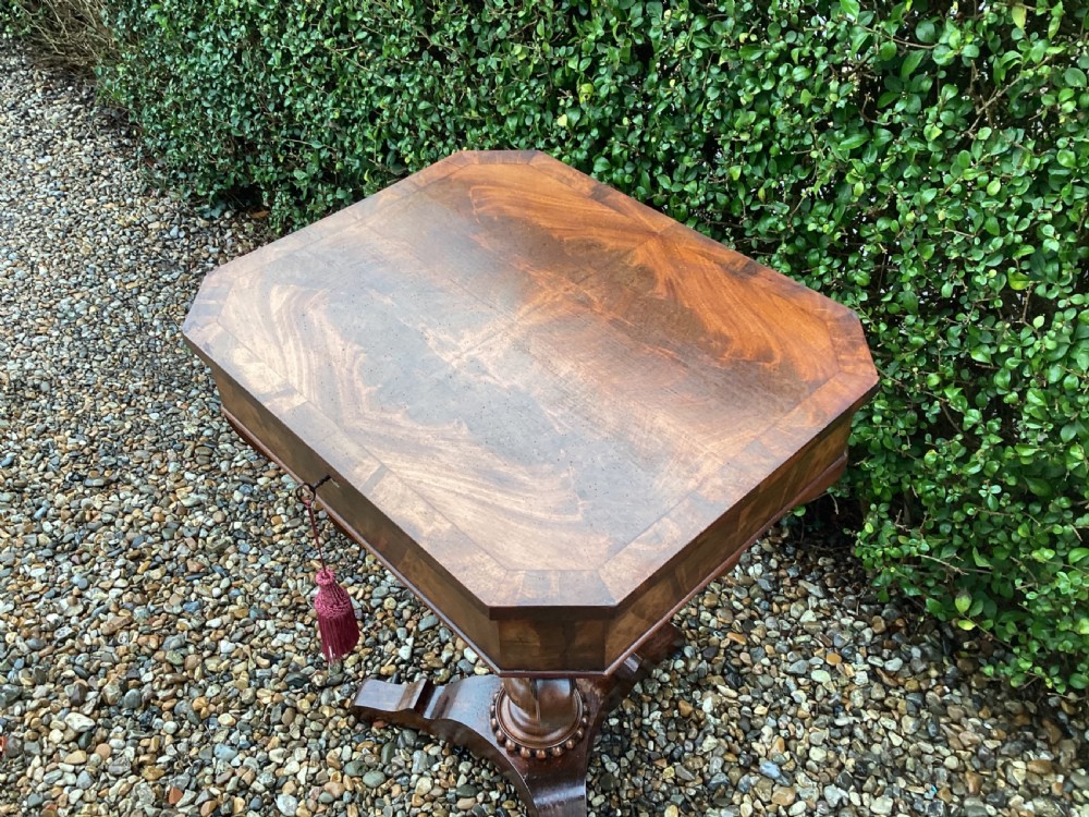 A Victorian flame mahogany sewing work table featuring a hinged top above a tapered work box, supported by curved S-scroll struts on a turned central pedestal with carved tripod legs. View XIV