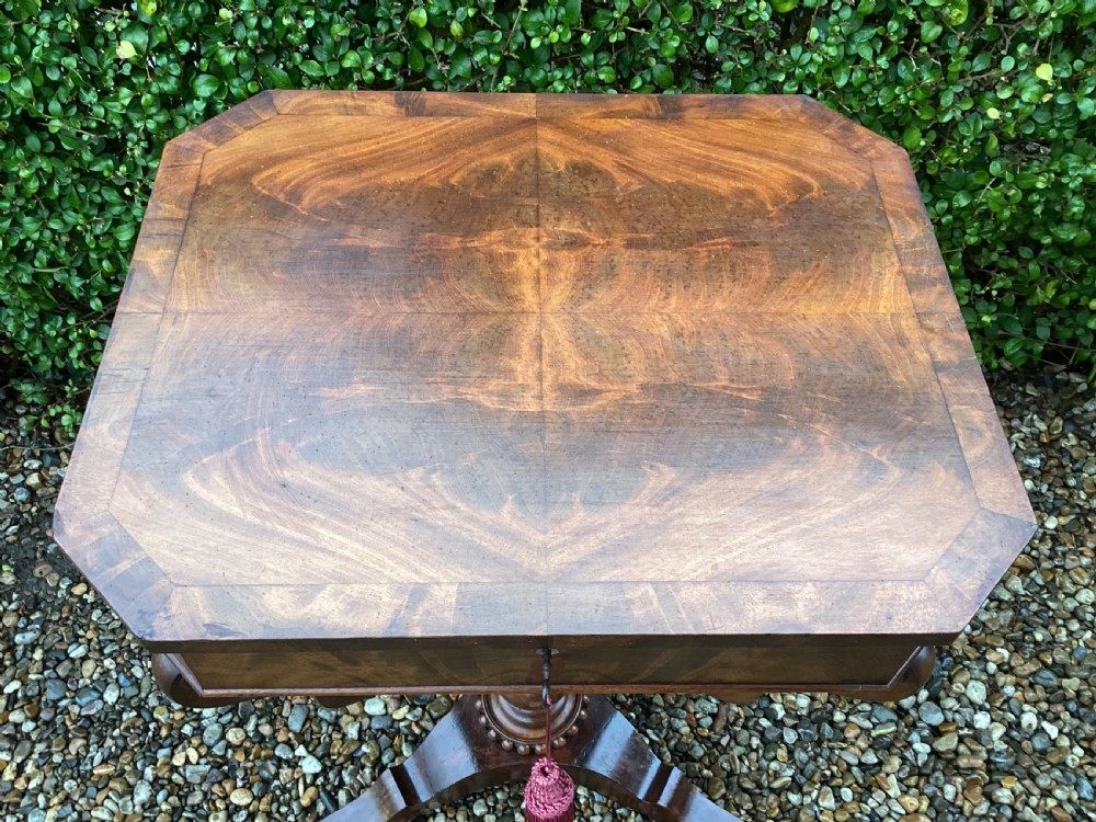 A Victorian flame mahogany sewing work table featuring a hinged top above a tapered work box, supported by curved S-scroll struts on a turned central pedestal with carved tripod legs. View XV