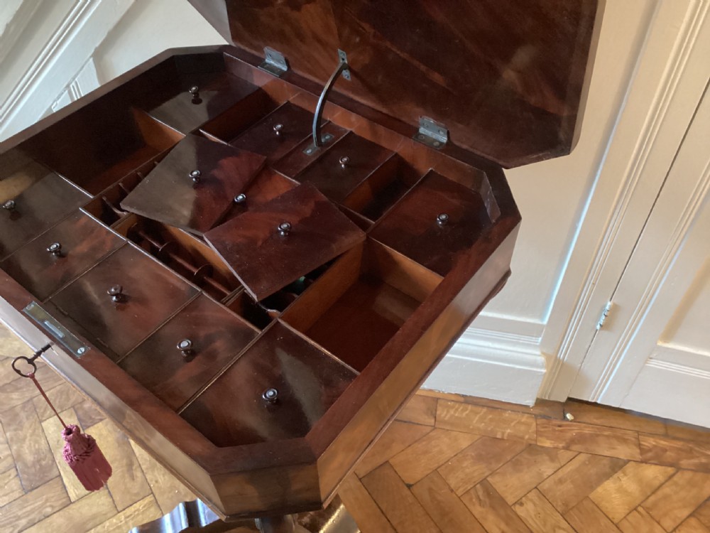 A Victorian flame mahogany sewing work table featuring a hinged top above a tapered work box, supported by curved S-scroll struts on a turned central pedestal with carved tripod legs. View XVIII