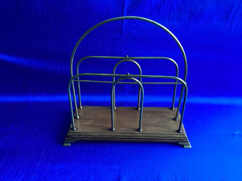 An Edwardian magazine rack featuring arched brass wire dividers mounted on a rectangular oak base with brass bracket feet.