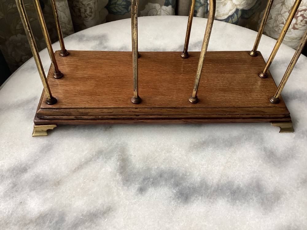 An Edwardian magazine rack featuring arched brass wire dividers mounted on a rectangular oak base with brass bracket feet. View VIII