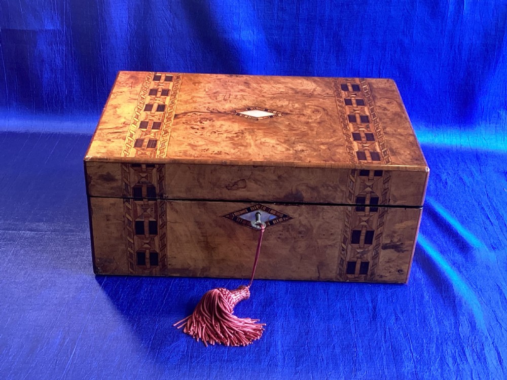 A closed Victorian burr walnut writing slope box decorated with geometric parquetry inlay bands and a central diamond keyhole escutcheon.