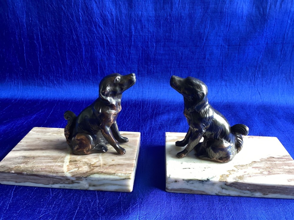 A pair of antique Art Deco bookends featuring patinated metal spaniel dogs sitting atop rectangular veined marble bases.