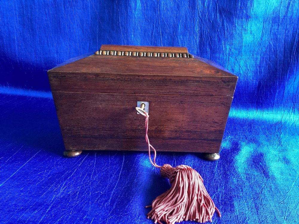 A Victorian rosewood tea caddy featuring a tapered sarcophagus lid with carved bead moulding, turned bun feet, and a central brass keyhole with a key and tassel.