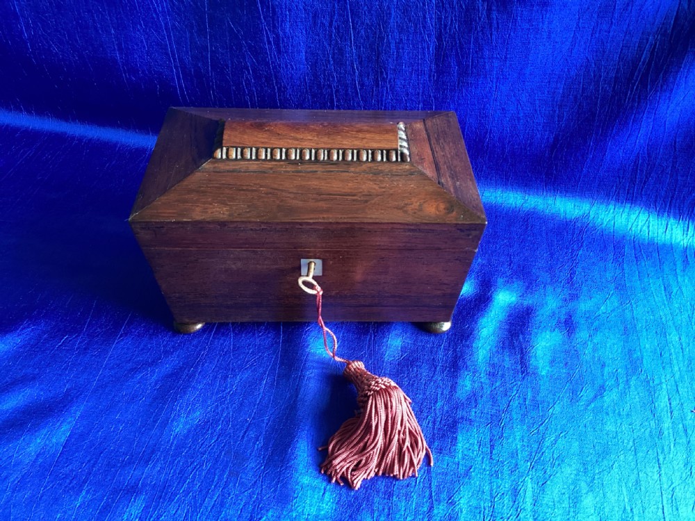 A Victorian rosewood tea caddy featuring a tapered sarcophagus lid with carved bead moulding, turned bun feet, and a central brass keyhole with a key and tassel. View II