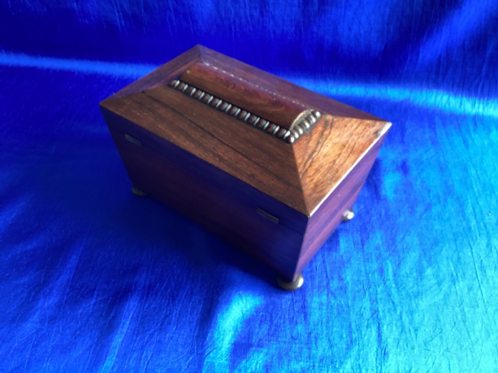 A Victorian rosewood tea caddy featuring a tapered sarcophagus lid with carved bead moulding, turned bun feet, and a central brass keyhole with a key and tassel. View IV