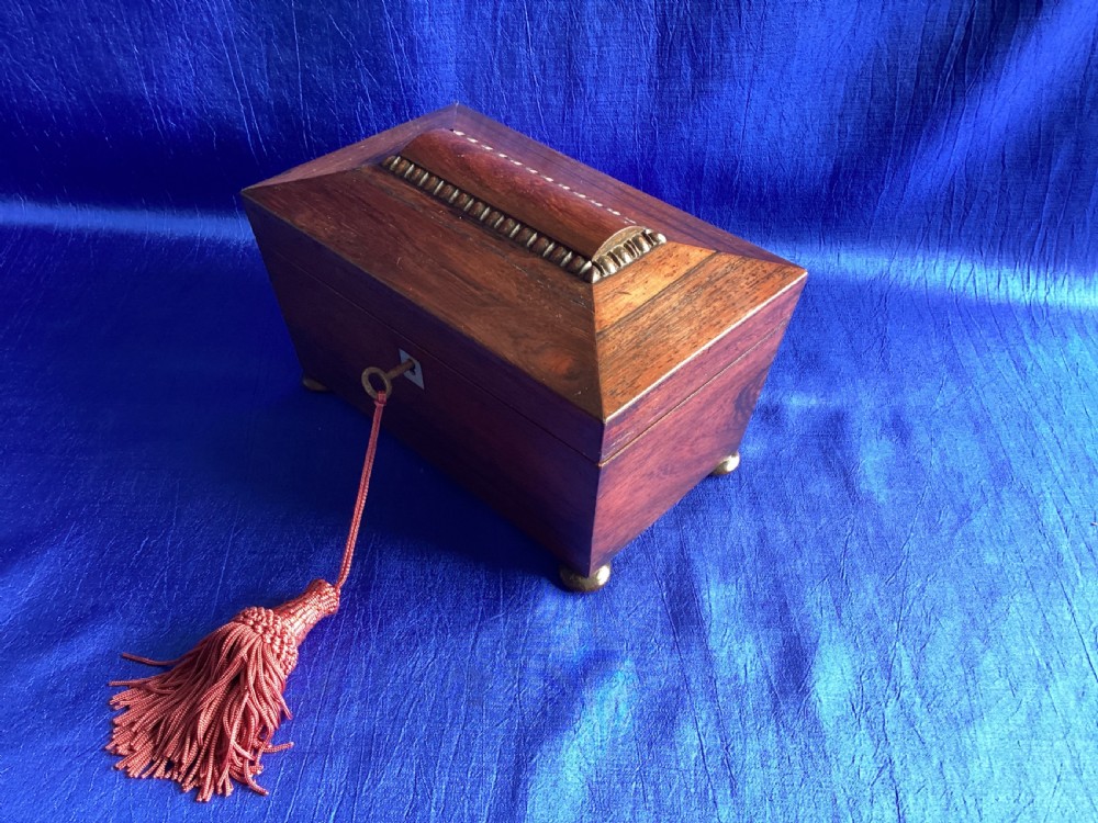 A Victorian rosewood tea caddy featuring a tapered sarcophagus lid with carved bead moulding, turned bun feet, and a central brass keyhole with a key and tassel. View VI