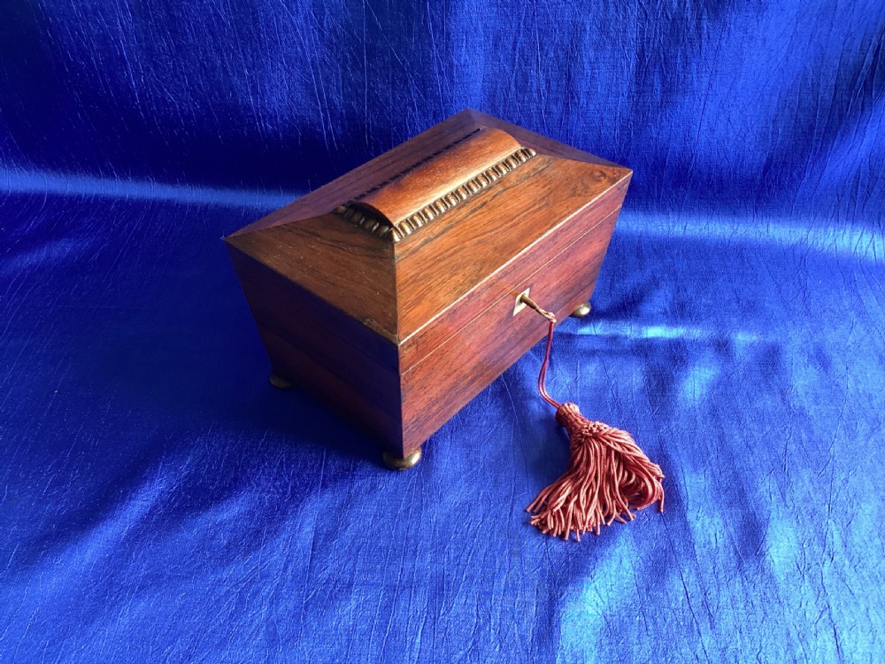 A Victorian rosewood tea caddy featuring a tapered sarcophagus lid with carved bead moulding, turned bun feet, and a central brass keyhole with a key and tassel. View VII