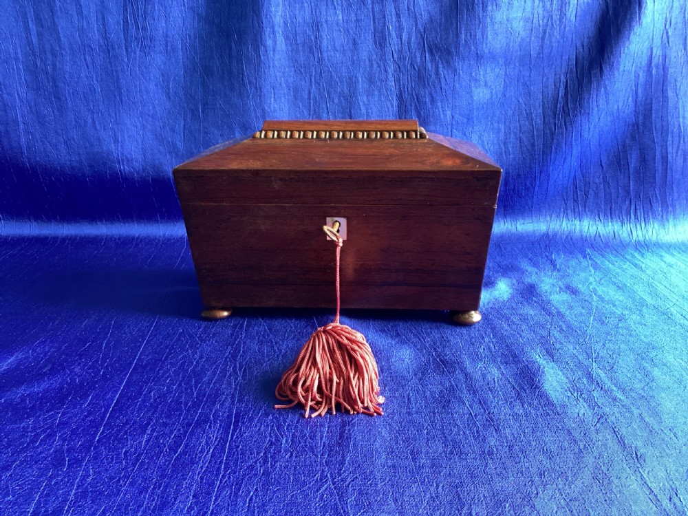 A Victorian rosewood tea caddy featuring a tapered sarcophagus lid with carved bead moulding, turned bun feet, and a central brass keyhole with a key and tassel. View IX