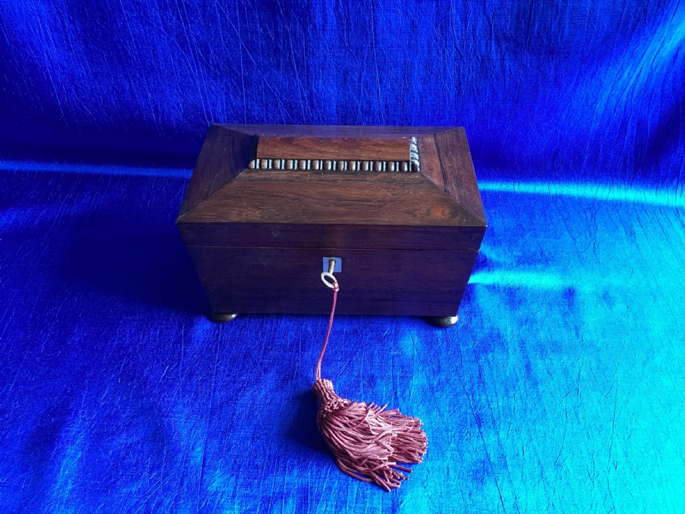 A Victorian rosewood tea caddy featuring a tapered sarcophagus lid with carved bead moulding, turned bun feet, and a central brass keyhole with a key and tassel. View XI