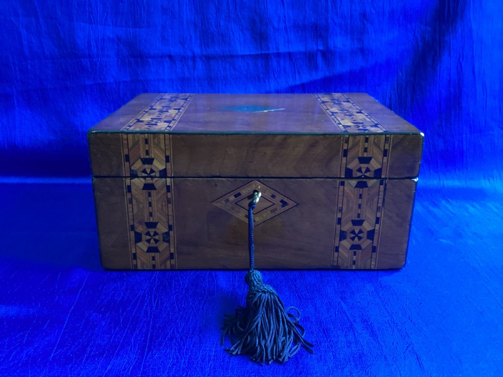 A Victorian walnut box featuring geometric parquetry inlay bands, a central diamond mother-of-pearl accent, and a tassel attached to the keyhole.