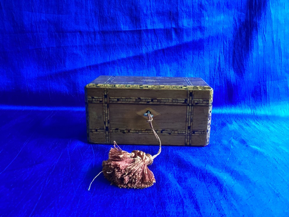 A rectangular Victorian walnut tea caddy featuring geometric parquetry inlaid borders, a central diamond-shaped keyhole escutcheon, and a key with a tassel.