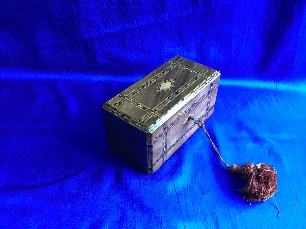 A rectangular Victorian walnut tea caddy featuring geometric parquetry inlaid borders, a central diamond-shaped keyhole escutcheon, and a key with a tassel. View IV