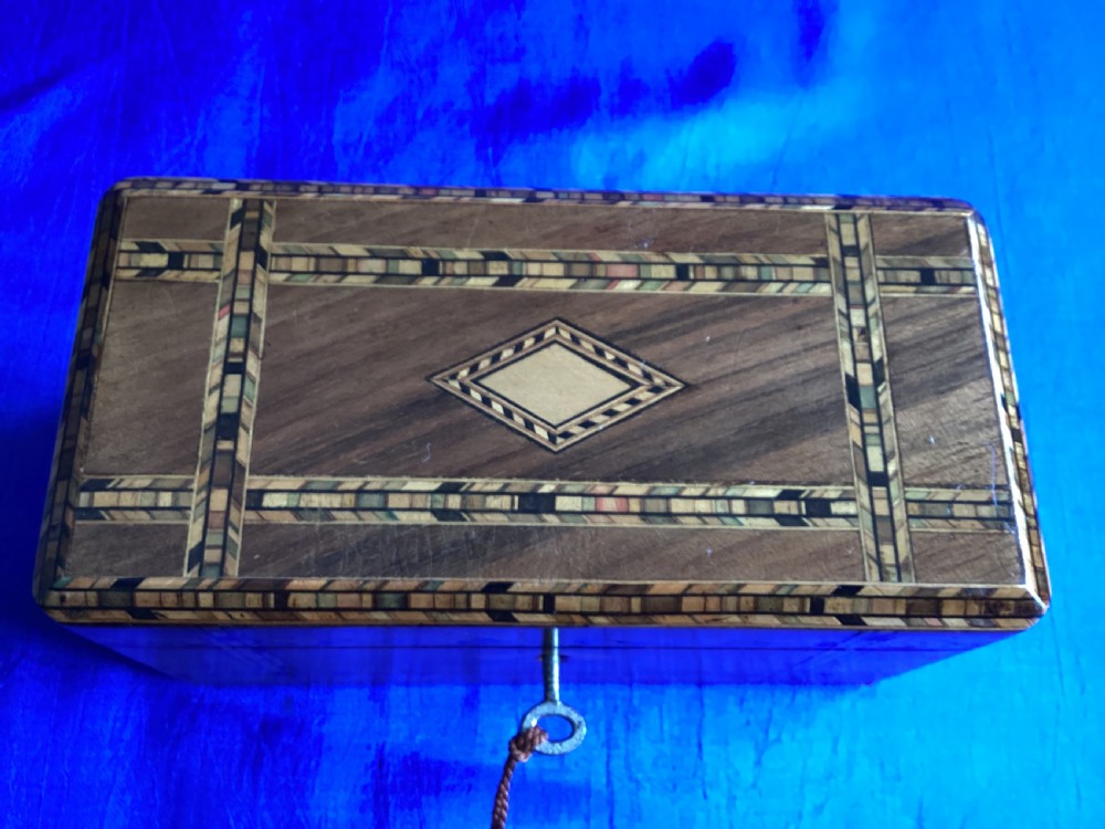 A rectangular Victorian walnut tea caddy featuring geometric parquetry inlaid borders, a central diamond-shaped keyhole escutcheon, and a key with a tassel. View V