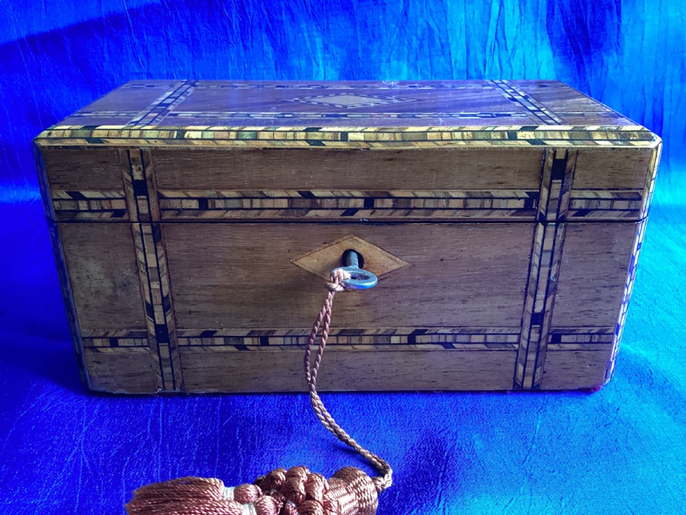 A rectangular Victorian walnut tea caddy featuring geometric parquetry inlaid borders, a central diamond-shaped keyhole escutcheon, and a key with a tassel. View VI