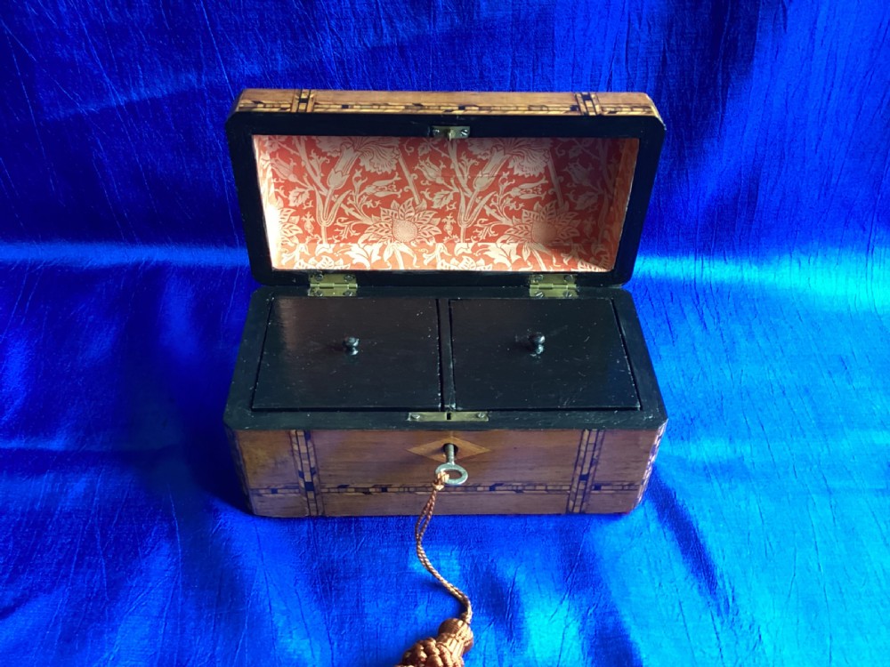 A rectangular Victorian walnut tea caddy featuring geometric parquetry inlaid borders, a central diamond-shaped keyhole escutcheon, and a key with a tassel. View VII