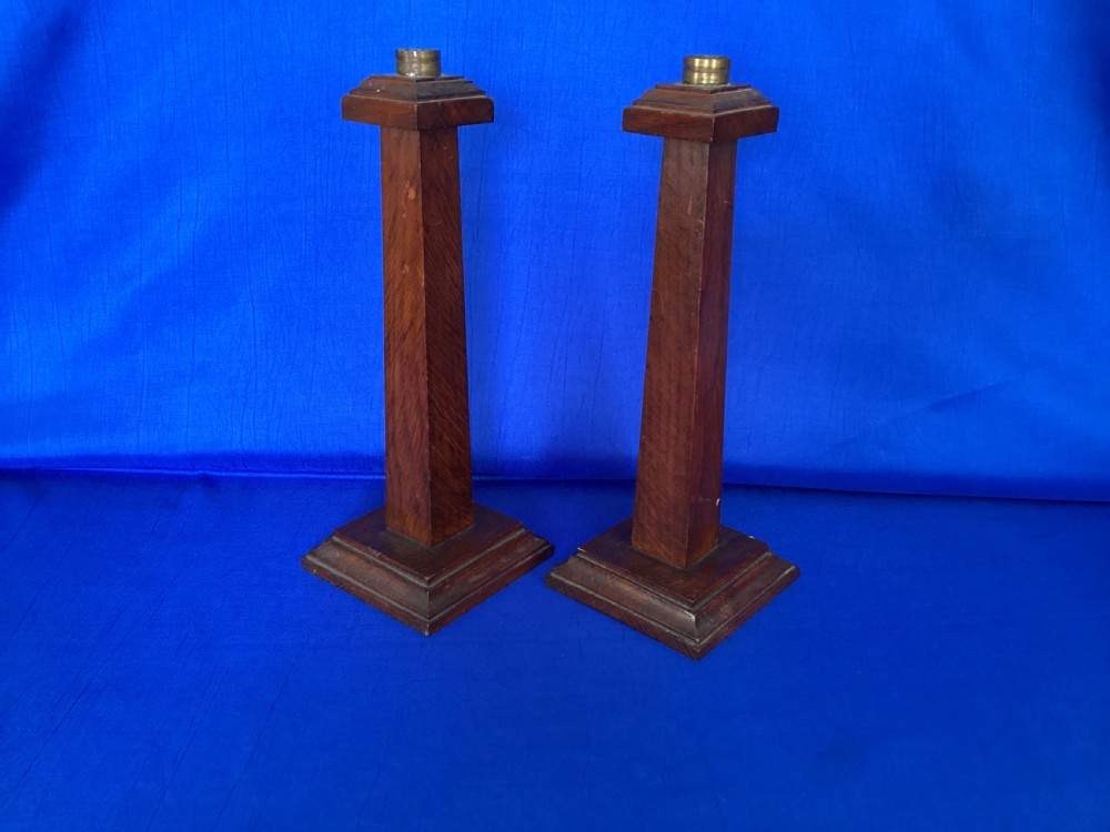 A pair of Edwardian Arts and Crafts tall oak candlesticks featuring square tapered shafts, stepped plinth bases, and brass nozzle inserts. View II