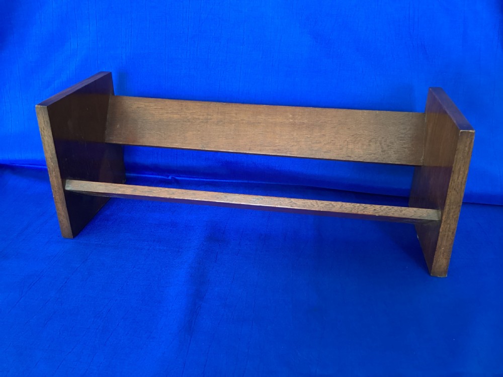A dark mahogany wooden book trough featuring angled shelf boards and rectangular side supports.
