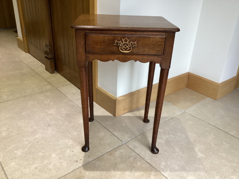 A Georgian country oak side table featuring a single drawer with a brass handle, shaped apron, and four tapered legs ending in pad feet.