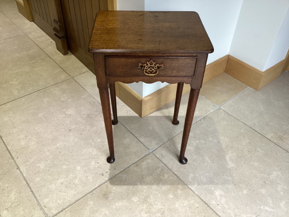 A Georgian country oak side table featuring a single drawer with a brass handle, shaped apron, and four tapered legs ending in pad feet. View II