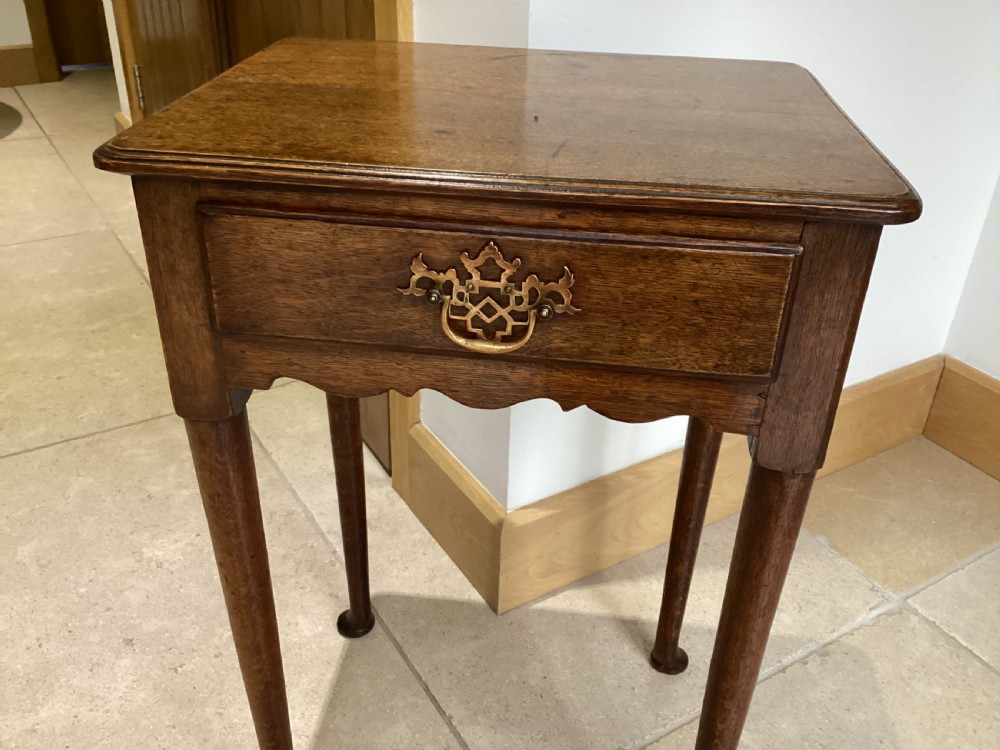 A Georgian country oak side table featuring a single drawer with a brass handle, shaped apron, and four tapered legs ending in pad feet. View V