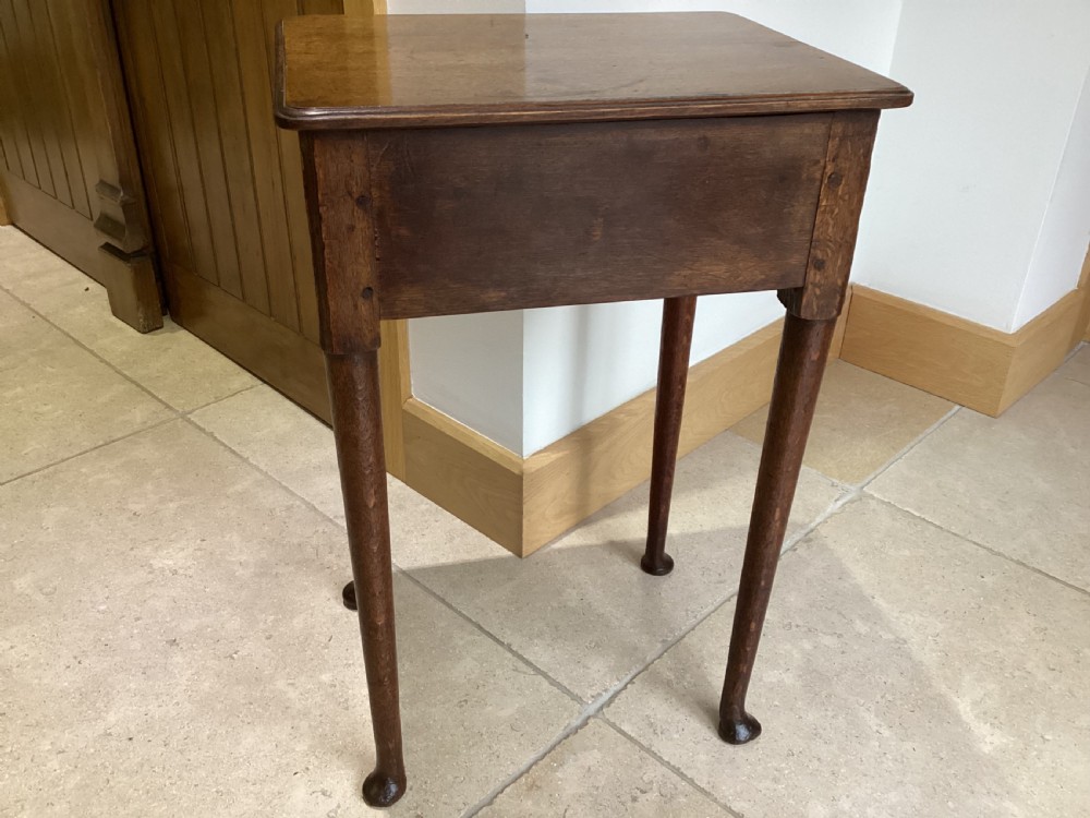 A Georgian country oak side table featuring a single drawer with a brass handle, shaped apron, and four tapered legs ending in pad feet. View VI