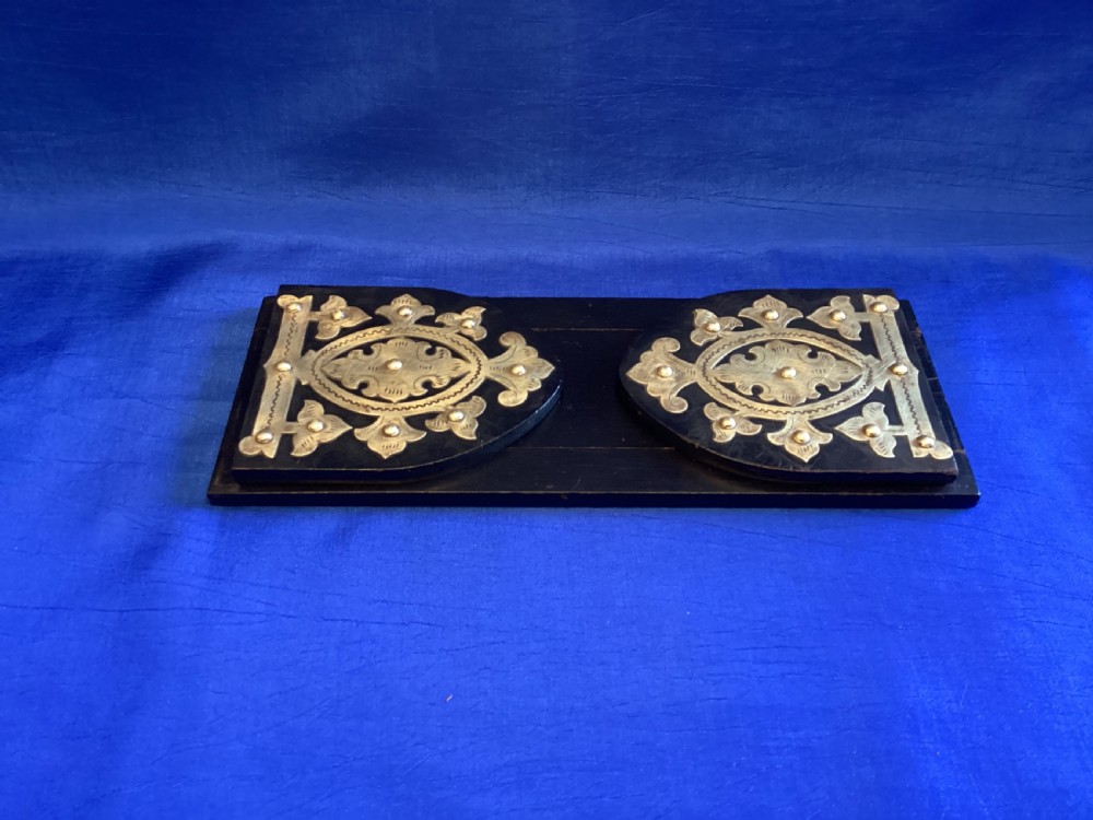 A Victorian black ebony extending book rest featuring hinged end supports decorated with ornate pierced brass strapwork.