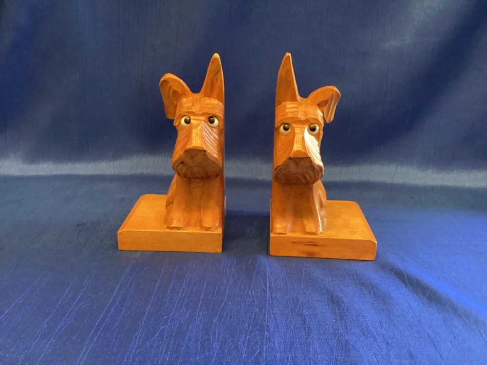 A pair of hand-carved wooden bookends shaped like Scottish Terriers with inset glass eyes on rectangular bases.