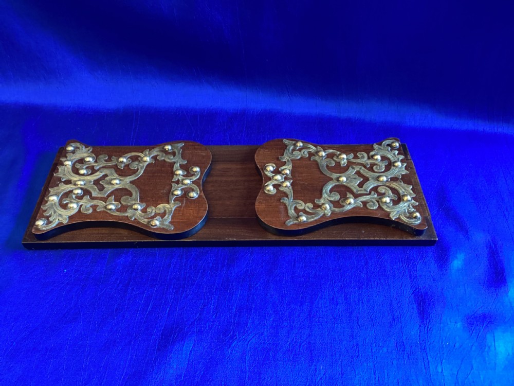 A dark mahogany extending book rest featuring decorative pierced brass scrollwork end panels with stud embellishments.