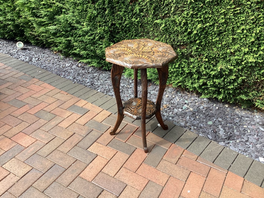 An antique dark wood octagonal side table featuring carved leaf patterns across the top surface, curved legs, and a lower tier shelf.
