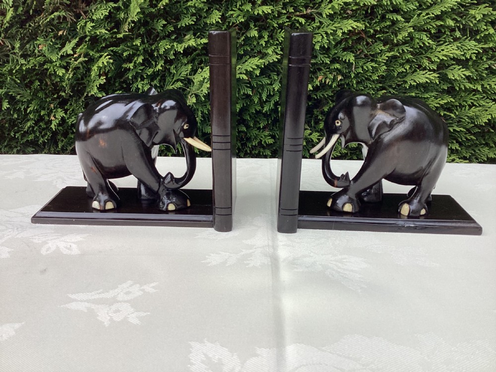 A pair of hand-carved dark coromandel wood elephant bookends featuring inlaid bone tusks and toes set on rectangular L-shaped bases.